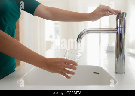 Femme remplissant verre d'eau à l'évier de cuisine, cropped Banque D'Images