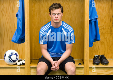 Jeune joueur de foot assis dans le vestiaire, portrait Banque D'Images