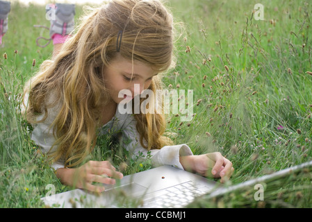 Girl lying in grass, regarder la coccinelle de ramper sur un ordinateur portable Banque D'Images