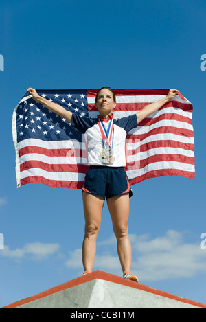 Athlète féminin à l'honneur sur le podium, holding up drapeau Américain Banque D'Images