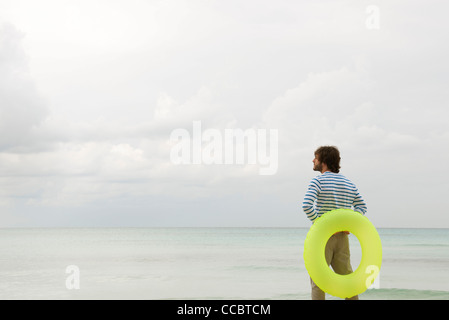 Jeune homme avec anneau gonflable, à la vue sur l'océan à Banque D'Images