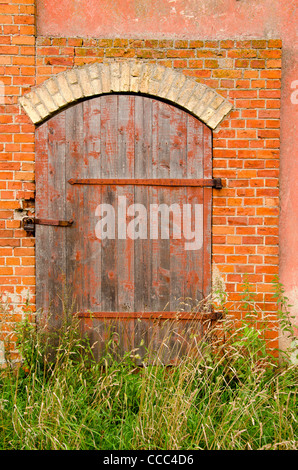 Ancien bâtiment de ferme abandonnée portières verrouillées avec serrure et les hautes herbes. Bâtiment en briques rouges de l'arrière-plan. Banque D'Images