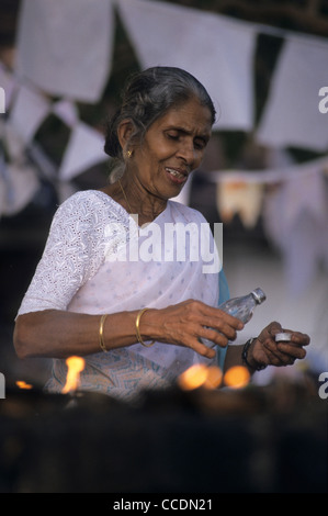 Vieille dame faire une offrande avec lampes à huile, cave temple, Dambulla, Sri Lanka Banque D'Images