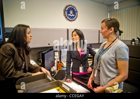 Les trois agents du FBI discuter d'un cas à Santa Ana, CA, bureau. Remarque Filipino-American en centre et logo fbi sur mur. Publié Banque D'Images