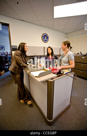 Les trois agents du FBI discuter d'un cas à Santa Ana, CA, bureau. Remarque Filipino-American en centre et logo fbi sur mur. Publié Banque D'Images