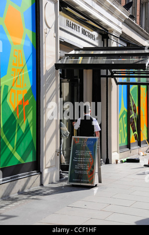 Portier à l'entrée du grand magasin Harvey Nichols & été haut en couleurs vente commerce Knightsbridge Londres Angleterre affiches fenêtre UK Banque D'Images