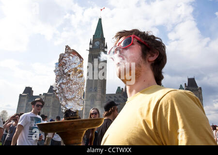 20 avril 2010 : avec la tour de la paix à l'arrière-plan, un jeune homme qui fume du cannabis au cours de la 420 un rassemblement sur la Colline du Parlement à Ottawa, Ontario, Canada. 420, 4:20 ou 4/20 (prononcé quatre-vingt) fait référence à la consommation de cannabis, et par extension, une façon de s'identifier aux drogues cannabis sous Banque D'Images