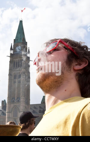 20 avril 2010 : avec la tour de la paix à l'arrière-plan, un jeune homme qui fume du cannabis au cours de la 420 un rassemblement sur la Colline du Parlement à Ottawa, Ontario, Canada. 420, 4:20 ou 4/20 (prononcé quatre-vingt) fait référence à la consommation de cannabis, et par extension, une façon de s'identifier aux drogues cannabis sous Banque D'Images