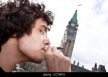 20 avril 2010 : avec la tour de la paix à l'arrière-plan, un jeune homme qui fume du cannabis au cours de la 420 un rassemblement sur la Colline du Parlement à Ottawa, Ontario, Canada. 420, 4:20 ou 4/20 (prononcé quatre-vingt) fait référence à la consommation de cannabis, et par extension, une façon de s'identifier aux drogues cannabis sous Banque D'Images