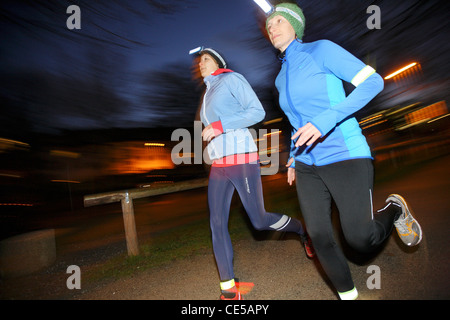 Deux jeunes femmes jogging la nuit en hiver, l'automne. Avec les projecteurs dans l'obscurité, sous l'étoffe. Banque D'Images