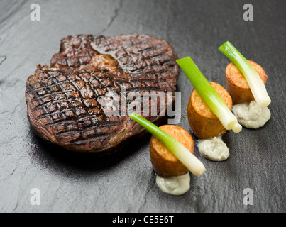 Un steak avec pommes de terre rôties et poireaux bébé Banque D'Images
