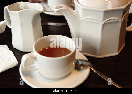 Une tasse de thé avec un nuage de lait et une théière en céramique Banque D'Images