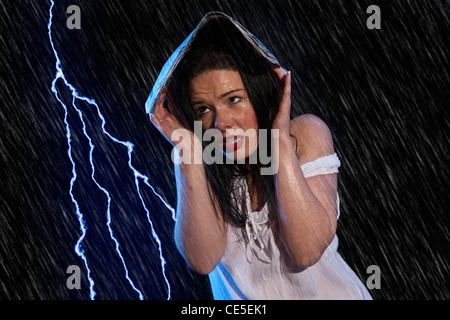 Une jeune femme abrite de la pluie sous un journal Banque D'Images