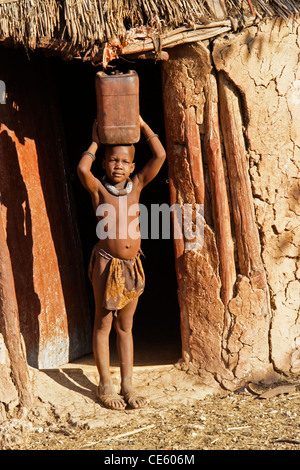 Jeune fille Himba portant de l'eau dans village près d'Opuwo, Namibie Banque D'Images