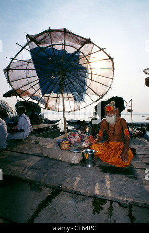 Sadhu priant sous le parapluie sur les ghats de la rivière Ganges ; Varanasi ; Uttar Pradesh ; Inde ; Asie Banque D'Images