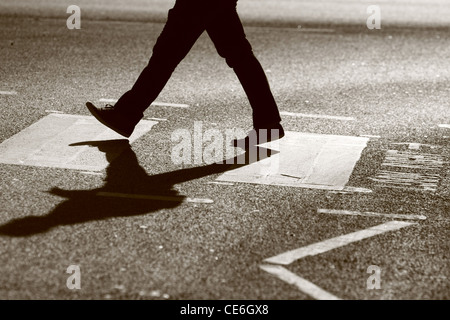 Les jambes d'un homme tel qu'il traverse une route à un passage clouté Banque D'Images