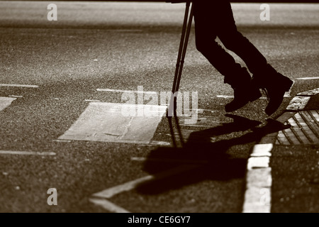 Les jambes d'un homme sur des béquilles qu'il traverse une route à un passage clouté Banque D'Images