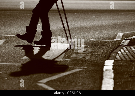 Les jambes d'un homme sur des béquilles qu'il traverse une route à un passage clouté Banque D'Images