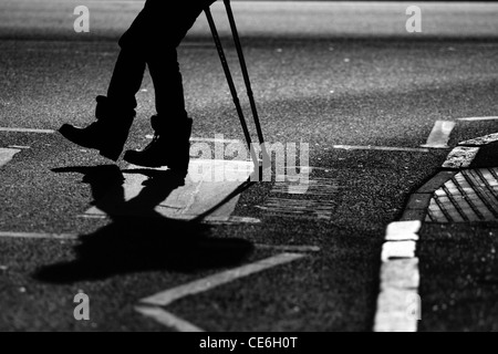 Les jambes d'un homme sur des béquilles qu'il traverse une route à un passage clouté Banque D'Images