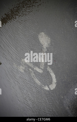 Panneau de stationnement peint pour les personnes handicapées sur l'asphalte recouvert d'eau par temps pluvieux Banque D'Images