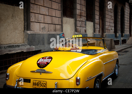 Vieille voiture américaine utilisée comme taxi avec un chauffeur sur son téléphone mobile portant un chapeau de cowboy. Bucanero annonce à la voiture. Drapeau cubain Banque D'Images