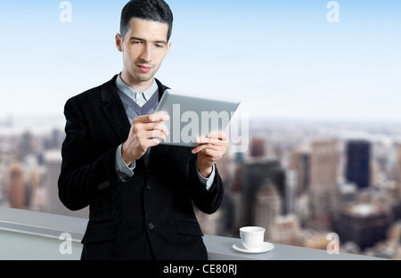 Jeune homme avec une tasse de café utilise une tablette numérique sur le toit d'un centre d'affaires. Cityscape floue avec des gratte-ciel Banque D'Images