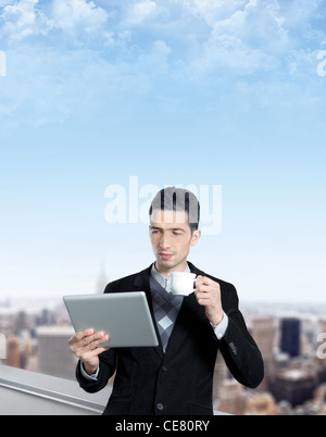 Jeune homme avec une tasse de café utilise une tablette numérique sur le toit d'un centre d'affaires. Cityscape floue avec des gratte-ciel Banque D'Images