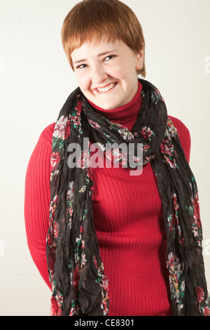 Souriante jeune femme rousse portant une chemise à col roulé rouge et foulard multicolore. Elle est à la fois chaleureux et heureux. Banque D'Images