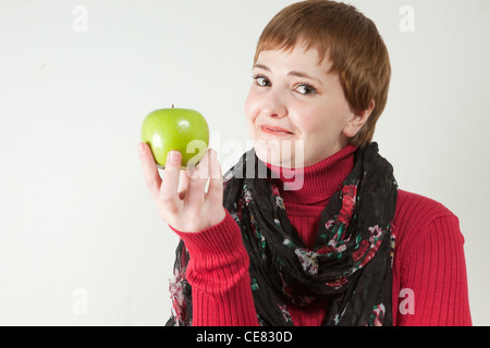 Les jeunes redhaired woman holding green apple en face d'elle, souriant à l'expression sur son visage. Banque D'Images