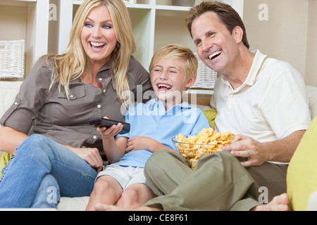 Un heureux, jeune famille de mère, père et fils, assis sur un canapé à regarder la télévision rire Banque D'Images