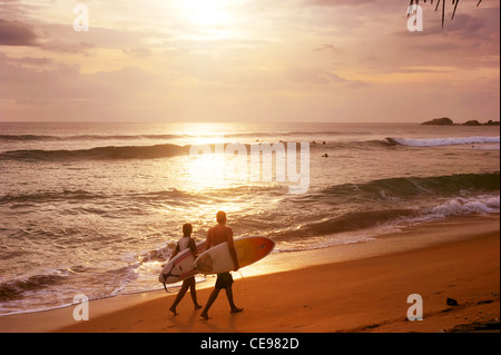 Couple de surfers promenades le long de la plage en Hikkaduva - est le deuxième meilleur surf paradise au Sri Lanka Banque D'Images