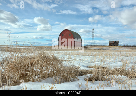 Une nouvelle grange rouge avec une vieille maison abandonnée et le moulin en arrière-plan. Banque D'Images