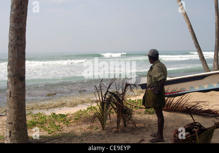 Un pêcheur se tenait près de son bateau sur la côte donne sur l'Océan Indien et les montres les vagues Banque D'Images