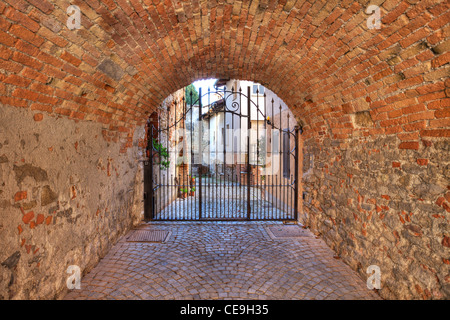 Passage voûté en briques anciennes menant vers metal gate à l'entrée de cour à La Morra, Italie. Banque D'Images