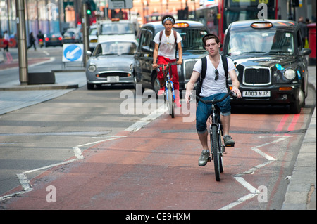 Les cyclistes et les taxis à l'aide d'une voie spéciale sur une route rouge road dans le centre de la ville de Londres, en Angleterre. Banque D'Images