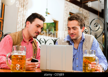 Deux amis en pub bavarois en vêtements traditionnels assis sur une table dans un pub avec coffre Banque D'Images