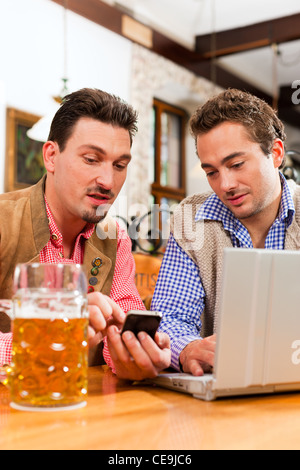Deux amis en pub bavarois en vêtements traditionnels assis sur une table dans un pub avec coffre Banque D'Images