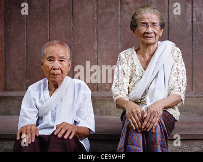 Portrait de deux vieilles femmes asiatiques assis contre le mur brun et looking at camera Banque D'Images