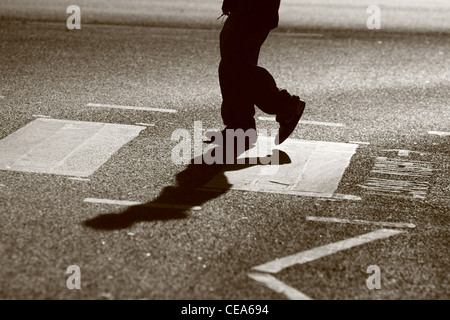 Les jambes d'un homme tel qu'il traverse une route à un passage piétons à Londres Banque D'Images