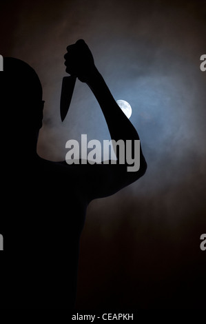 Silhouette d'homme avec un couteau à la recherche à la lune Banque D'Images