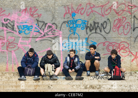 Les garçons assis en face d'un mur plein de graffitis sur les rues de Rome, Italie Banque D'Images