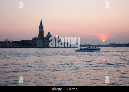 Venise, Vénétie, Italie. Au coucher du soleil Vue à travers lagune à la Chiesa di San Giorgio Maggiore, bateau qui passe. Banque D'Images