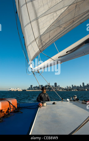 De partir de Pier 39 pour une croisière en catamaran au coucher du soleil avec l'horizon de la ville derrière le skipper. San Francisco. Banque D'Images