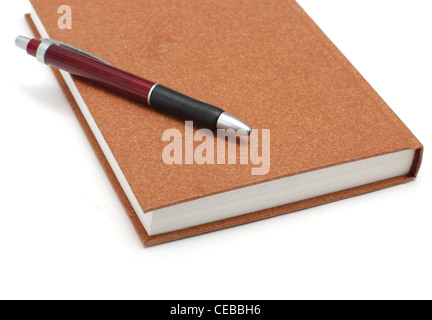 Agenda brun couché sur la surface avec un stylo blanc isolé sur fond blanc Banque D'Images