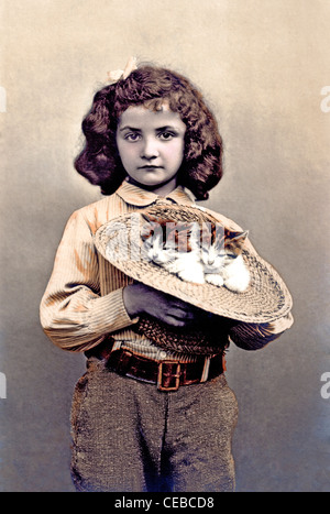 Vintage photo d'une jeune fille tenant une paire de chatons dans son chapeau de paille, vers 1910. Banque D'Images