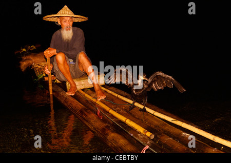 Le Cormorant fisherman holding bird sur une chaîne sur un radeau de bambou sur la rivière Li à Guilin, Yangshuo nuit Xingpingzhen Guangxi, Chine Banque D'Images