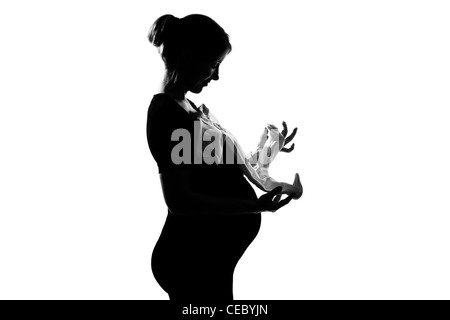 Une belle caucasian pregnant woman holding vêtements de bébé en silhouette sur fond blanc isolé studio Banque D'Images