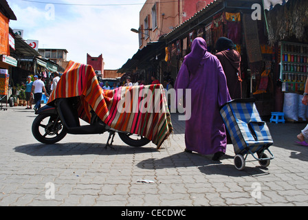 Femme avec panier en passant par scooter recouvert d'un tapis à Marrakech, Maroc Banque D'Images