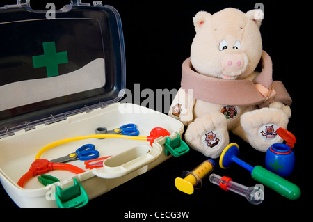 'Blessé' cochon adorable en peluche (bras en écharpe) et outils de son médecin's kit médical (cas ouvert, seringue, thermomètre, stéthoscope) - England, UK. Banque D'Images