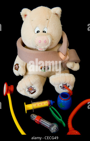 Cochon en peluche blessés isabelle (bras en écharpe) & seringue, stéthoscope, thermomètre de l'enfant médecin kit médical pour jeu de rôle jeu - England, UK. Banque D'Images